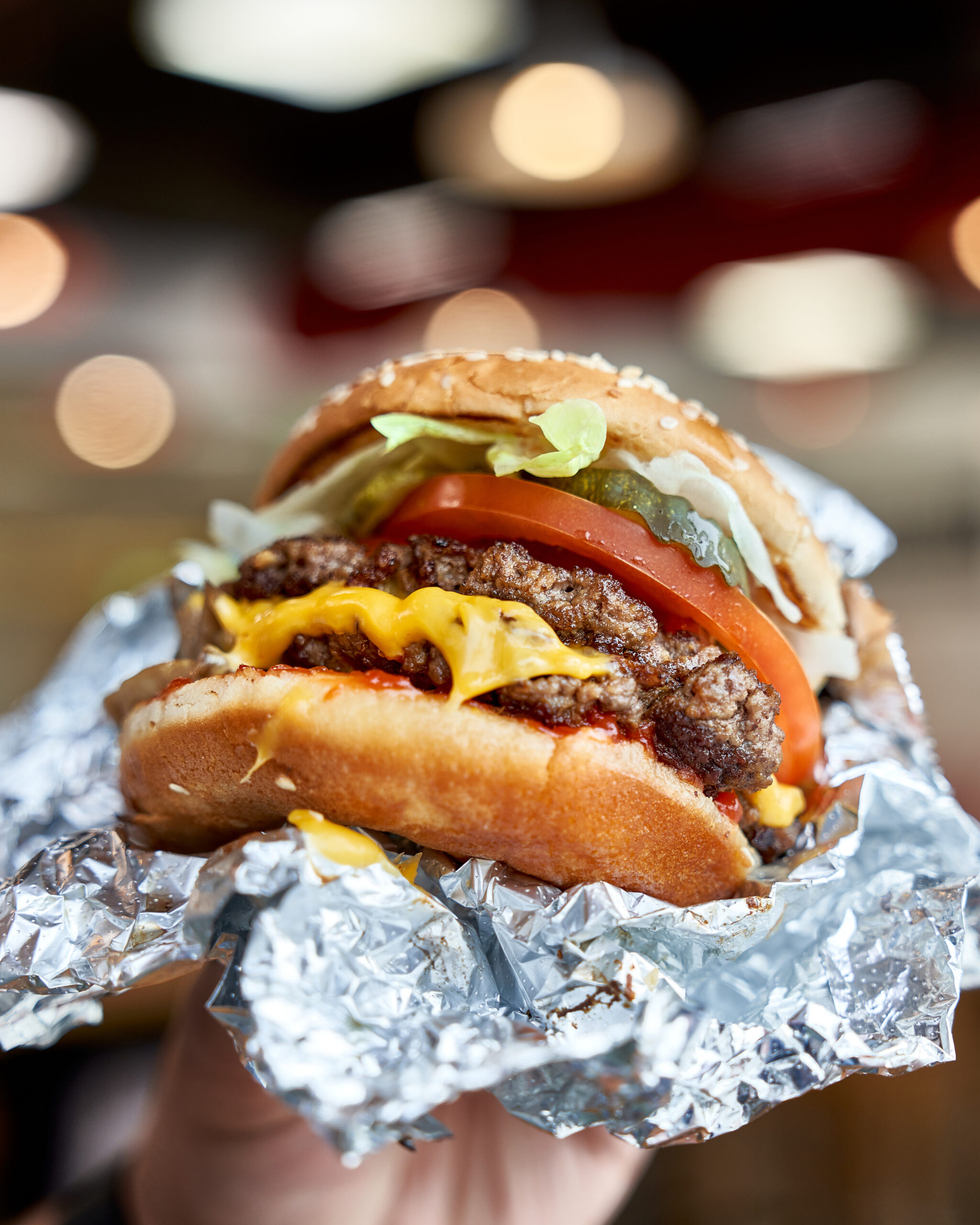 Five Guys cheeseburger partially wrapped in foil with lettuce and tomato.